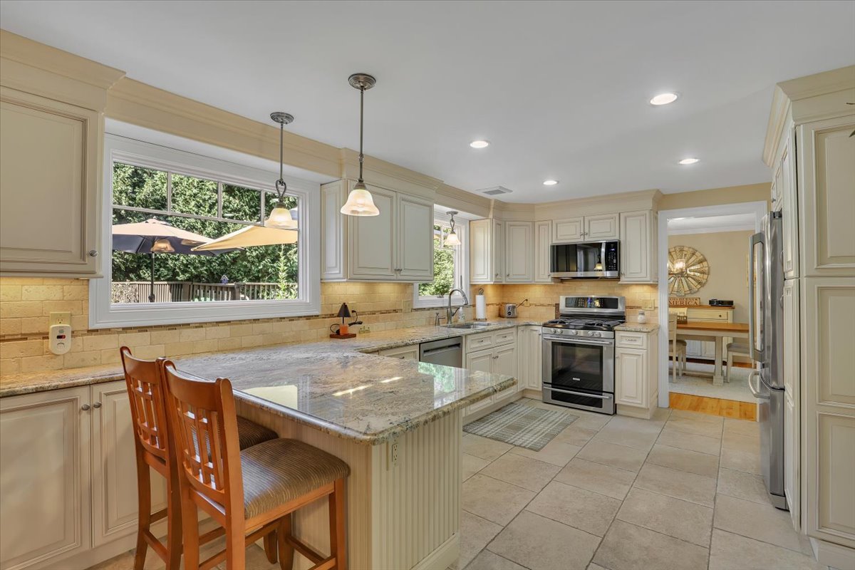 A view of a modern open-concept kitchen featuring granite countertops, a large peninsula with a breakfast bar and chairs, looking into a formal dining area.