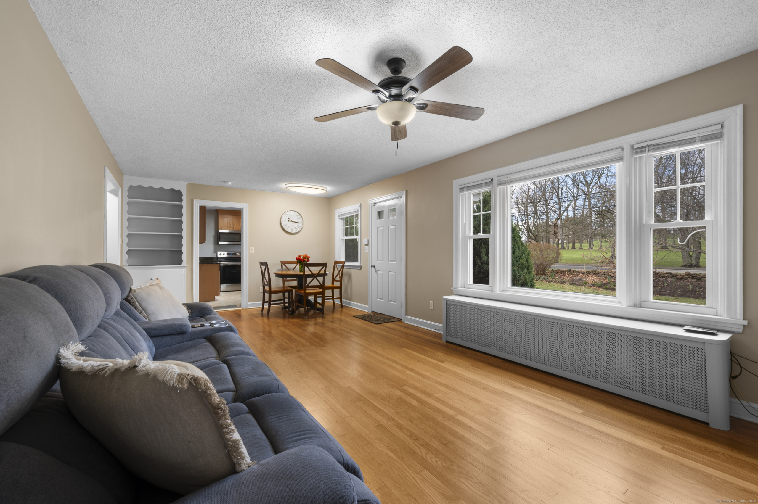 Spacious living room with oak hardwood floors, large windows, and a ceiling fan in Wallingford, CT.