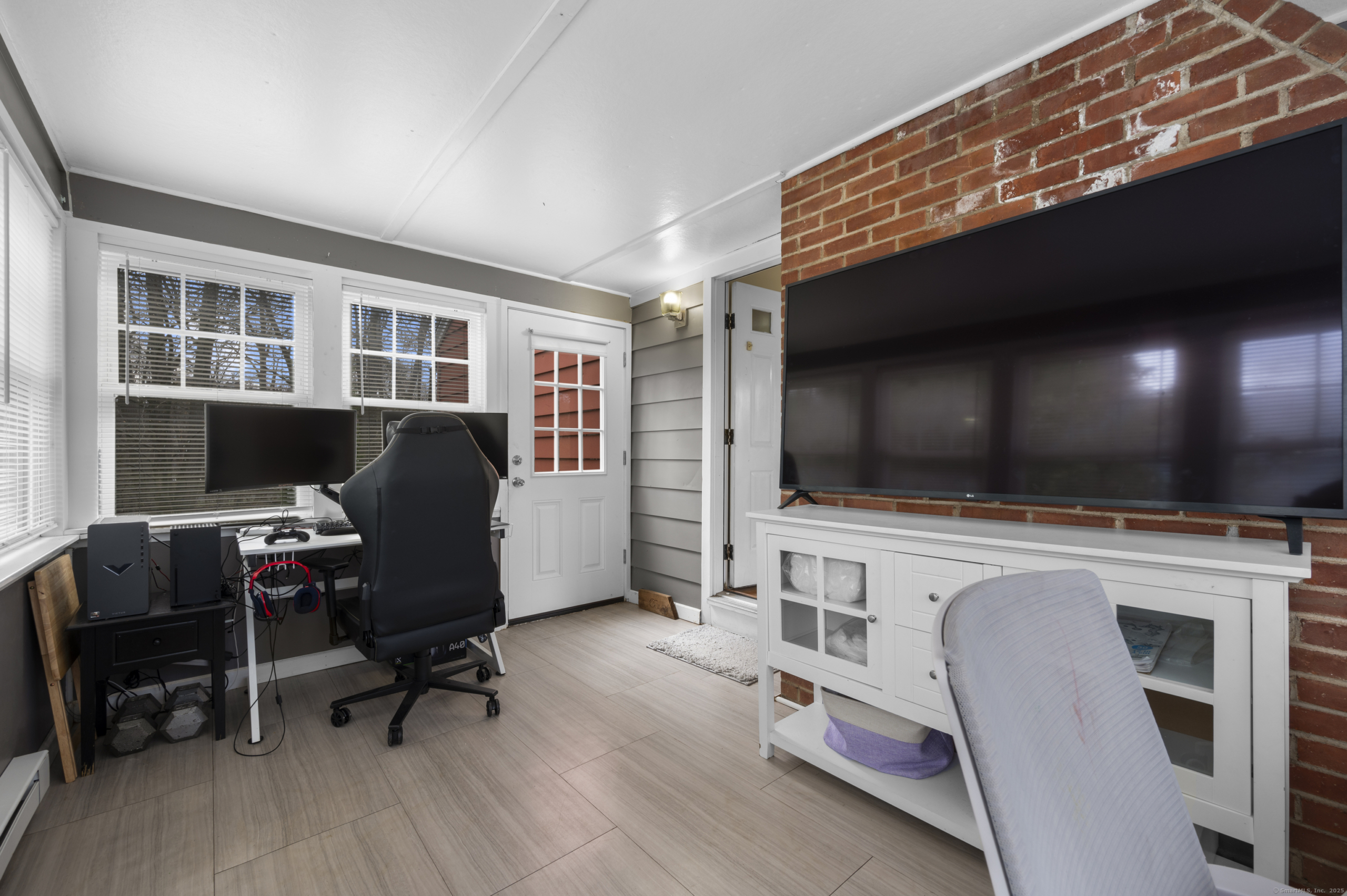 Finished sunroom or home office at 140 Woodhouse Ave with exposed brick accent wall and tile flooring.