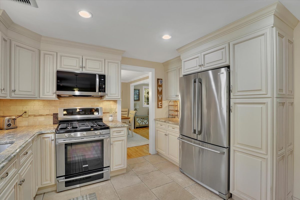 A comprehensive view of a chef's kitchen featuring cream-colored cabinets, granite countertops, and stainless steel appliances.