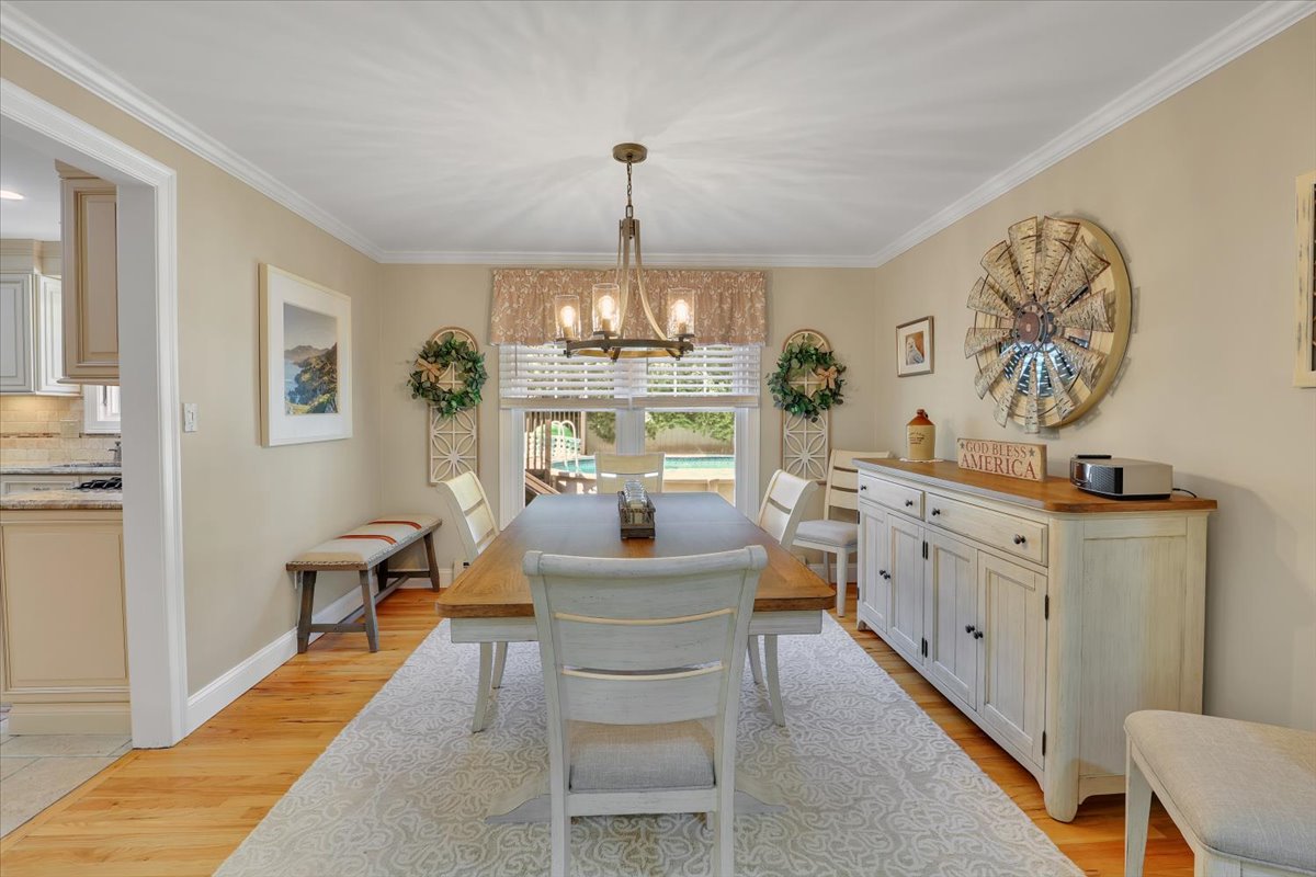 A formal dining room with a large farmhouse table, a rustic iron chandelier, a sideboard, and decorative wreaths on a light beige wall.