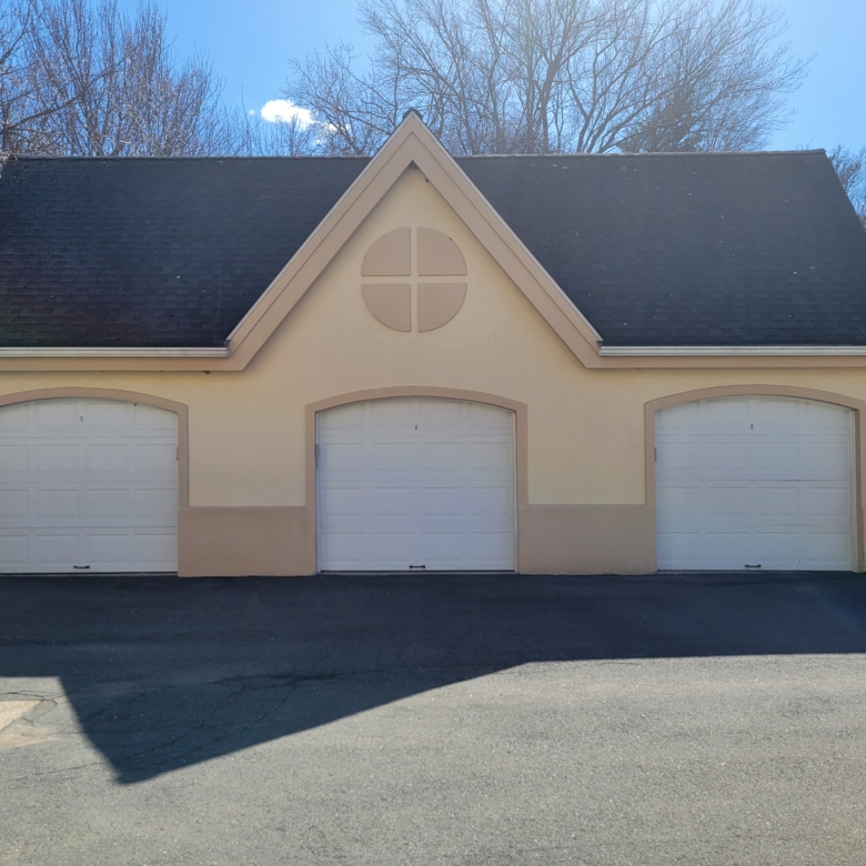 Exterior view of a tan, three-bay detached oversized garage with a gabled roof and decorative circular detail.