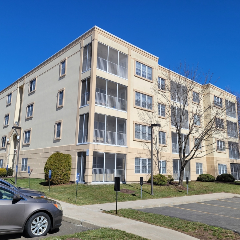 Modern multi-story apartment building with tan stucco siding and numerous screened-in balconies under a bright blue sky.