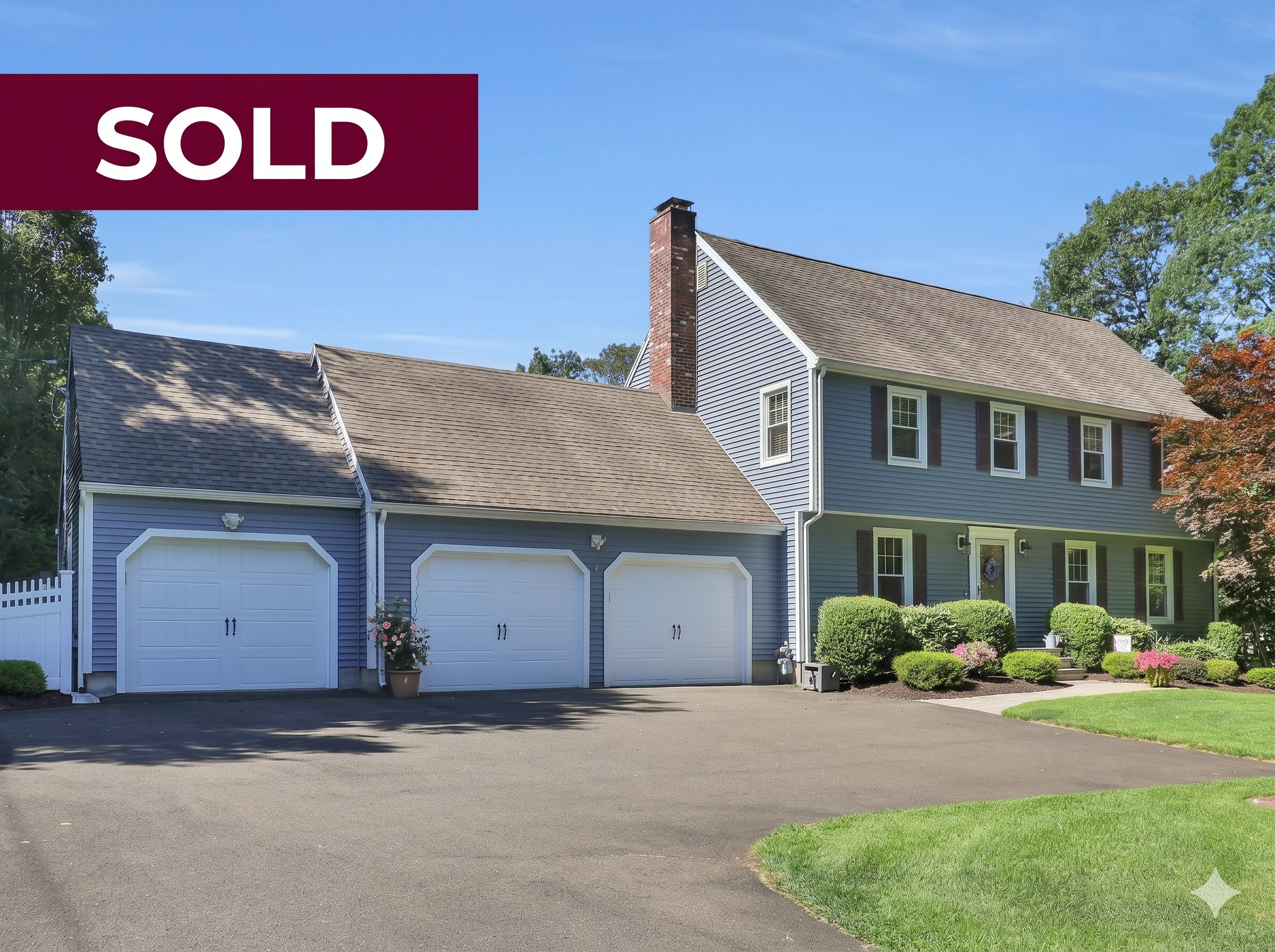 Front view of a stately two-story colonial-style single-family home with blue siding, a three-car attached garage, a large asphalt driveway, manicured green landscaping, and a red brick chimney on a sunny day, featuring a large "SOLD" banner overlay in the upper left corner.