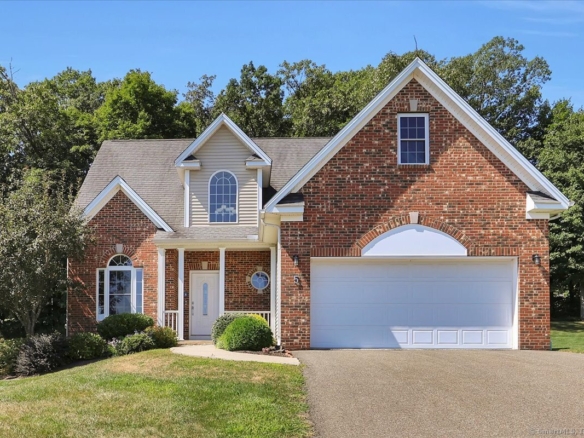Exterior front view of a multi-story red brick colonial house at 5 Sonoma Ln with an attached two-car garage, manicured green lawn, and arched window accent.