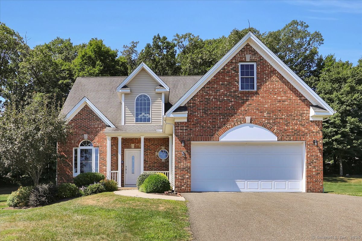 Exterior front view of a multi-story red brick colonial house at 5 Sonoma Ln with an attached two-car garage, manicured green lawn, and arched window accent.