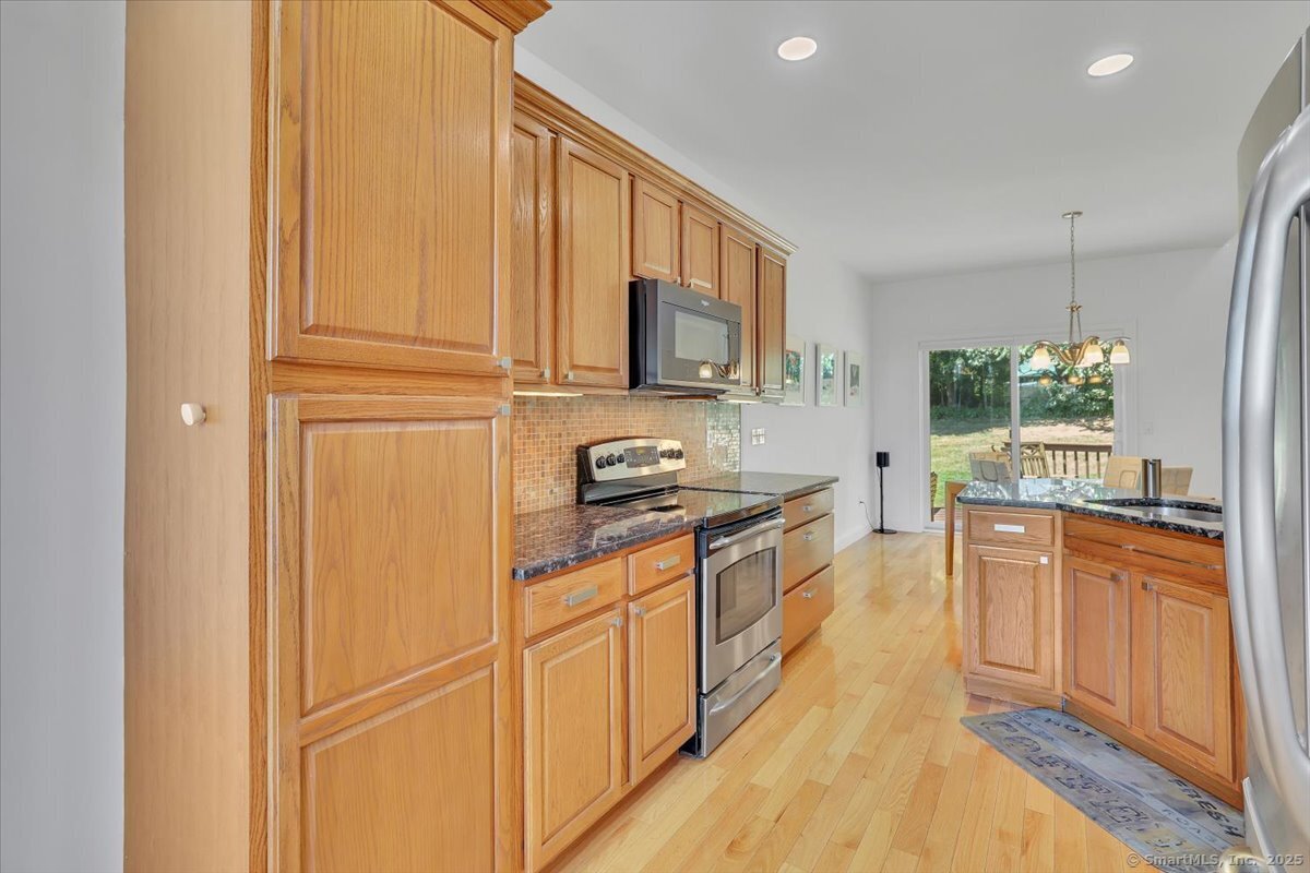 Modern kitchen with custom honey oak wood cabinets, dark granite countertops, stainless steel appliances, and a view out the sliding glass patio door.