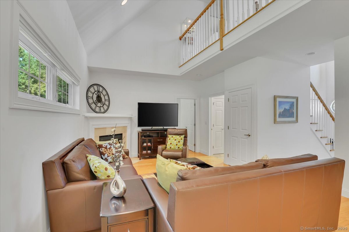 Spacious living room at 5 Sonoma Ln featuring a vaulted ceiling, brown leather sofas, a corner fireplace, a wall-mounted TV, and a view of an open second-floor loft railing.