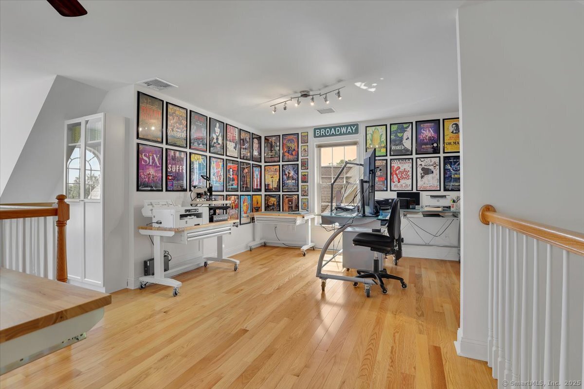 Large second-floor open loft area utilized as a home office, featuring hardwood floors, a computer desk, and walls covered in framed Broadway posters.