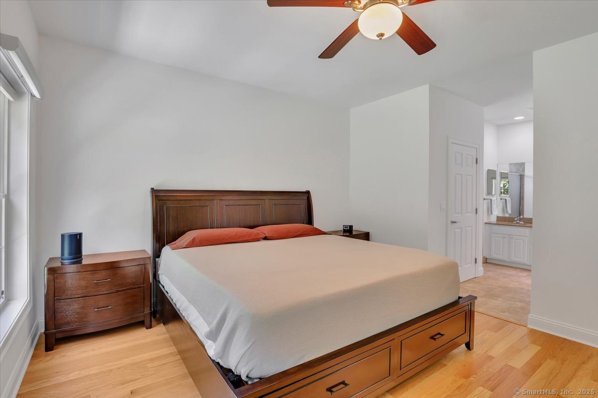 Spacious primary bedroom suite with an elegant dark wood bed frame, hardwood flooring, a ceiling fan, and a master bathroom visible through a wide doorway.