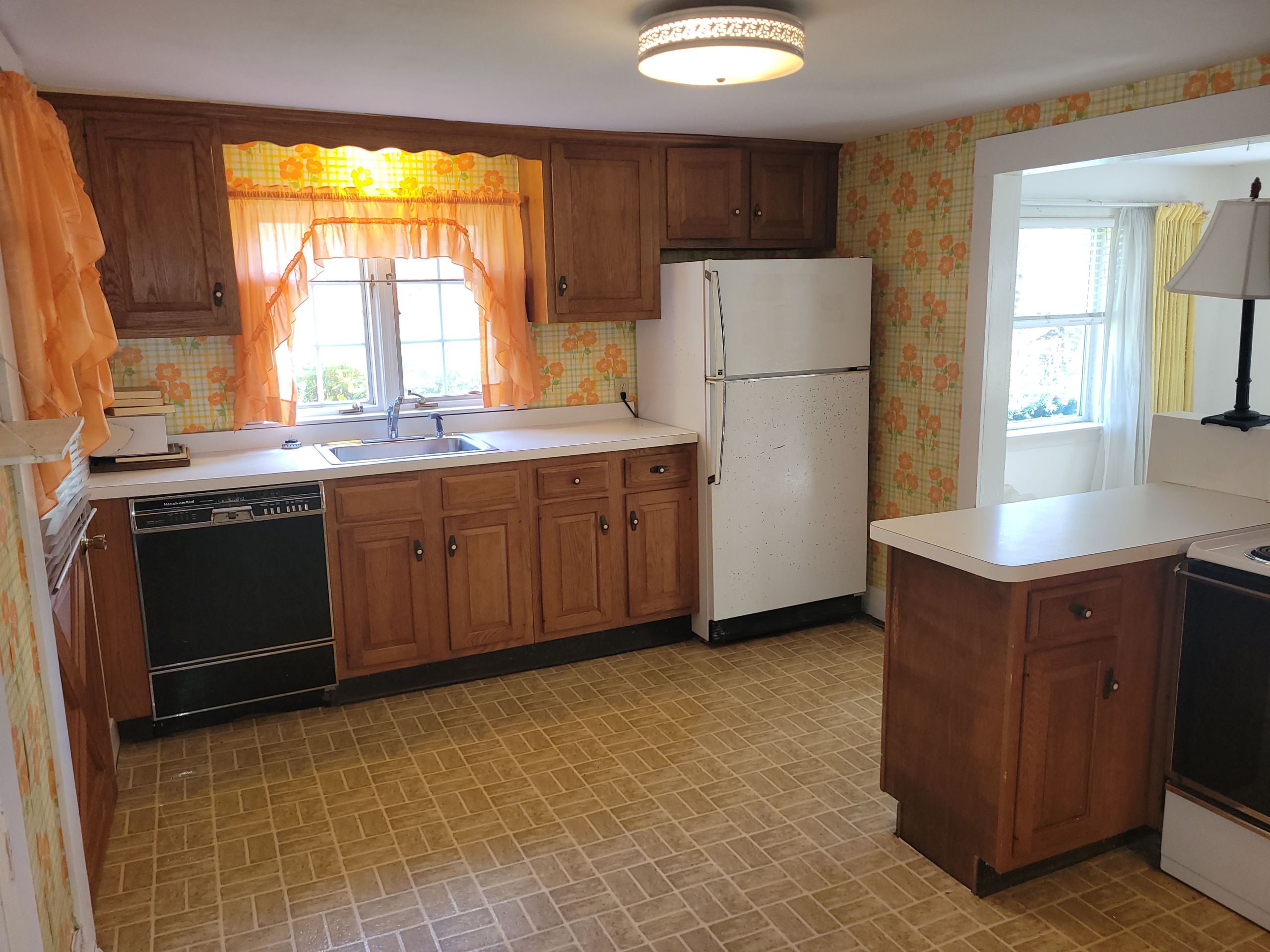 Kitchen sink area at 60 Chestnut Lane with wood cabinets, dishwasher, and vintage floral wallpaper.
