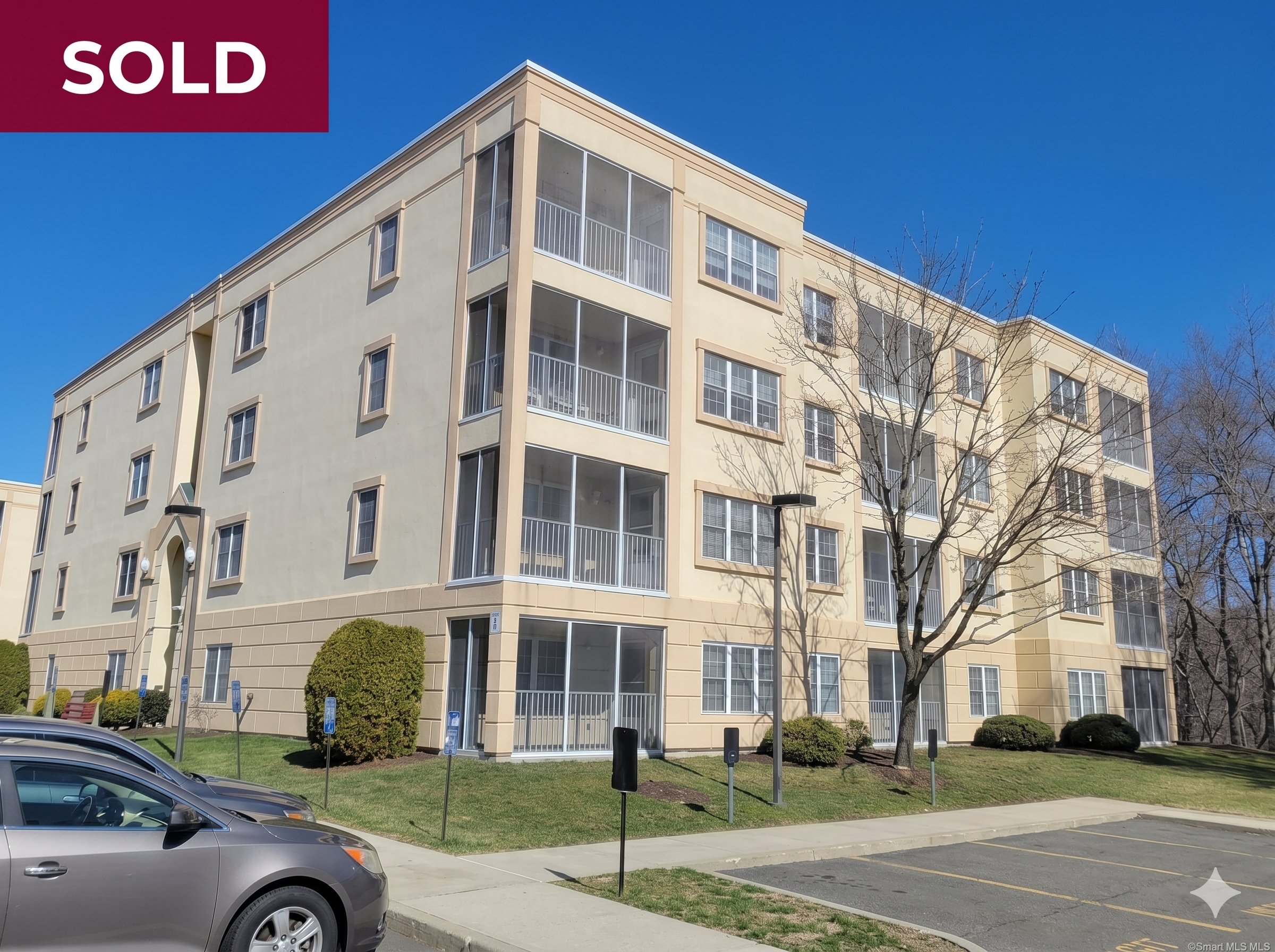 Exterior view of a modern four-story beige condominium building at The Commons at Mill River, a 55+ community located at 75 Washington Avenue, Hamden, CT.
