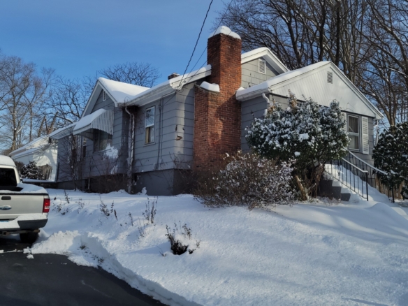 Side exterior of 78 Summit St, Meriden, CT, featuring gray siding, a large brick chimney, and a snowy driveway.