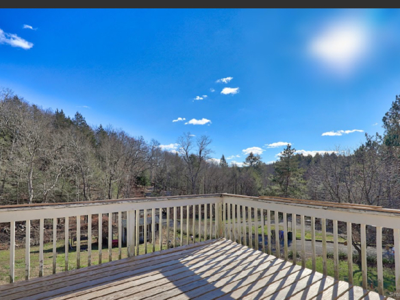 View from the wooden deck at 1101 Hickory Hill Road, Thomaston, looking out toward distant hills and a clear blue sky.