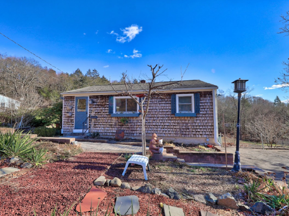 Front view of the cedar shake home at 1101 Hickory Hill Road, Thomaston, CT, with blue shutters and a stone-lined garden bed.