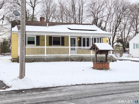 Centered view of a yellow home featuring a white covered porch and black shutters on the windows.