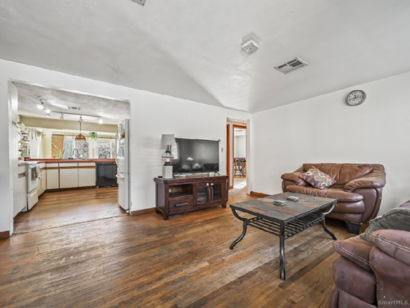 Interior view of the living room featuring original hardwood floors and an open-concept flow into the kitchen area.
