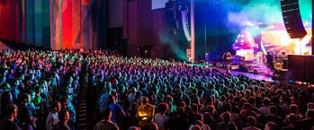 A vibrant, crowded concert at the Toyota Oakdale Theatre in Wallingford, CT, featuring a brightly lit stage with a large purple mushroom prop and a full audience in the auditorium.