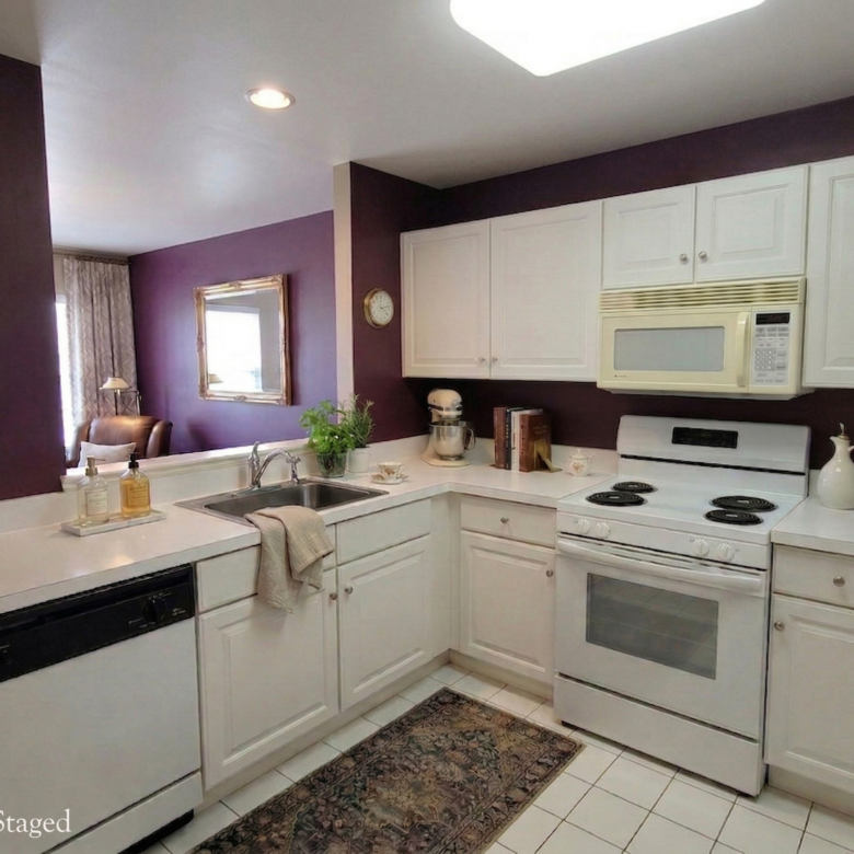 A kitchen featuring white cabinetry, white appliances including a Kitchen view showing the white countertops and a pass-through window looking into the living area with purple walls.range, and a deep purple accent wall.