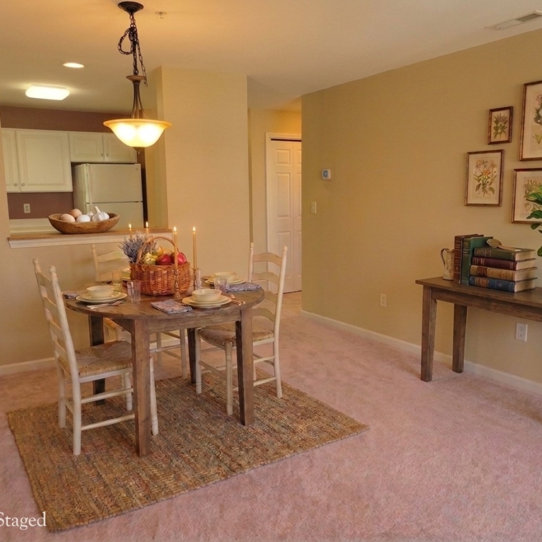 A dining area with a round wooden table, tan walls, and a view through to the kitchen and hallway.
