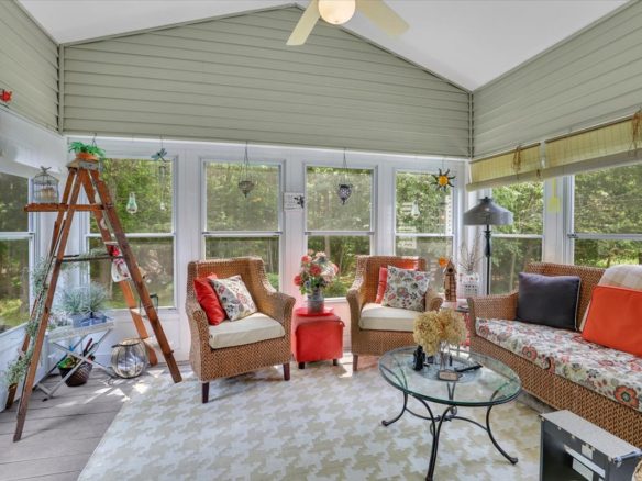 Bright sunroom with wrap-around windows, wicker furniture, and a tray ceiling at 33 Wadsworth Lane.