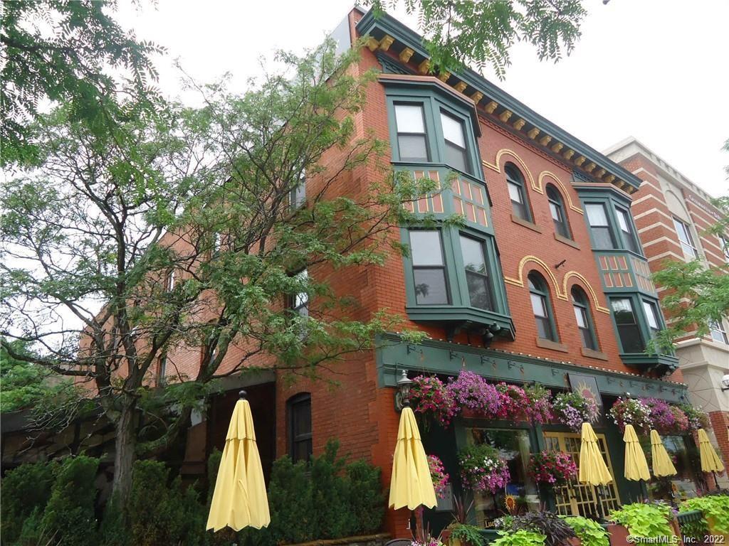 Exterior view of a historic brick apartment building located at 489 Main Street in Middletown, CT, featuring charming architectural details, large bay windows, and vibrant hanging flower baskets.