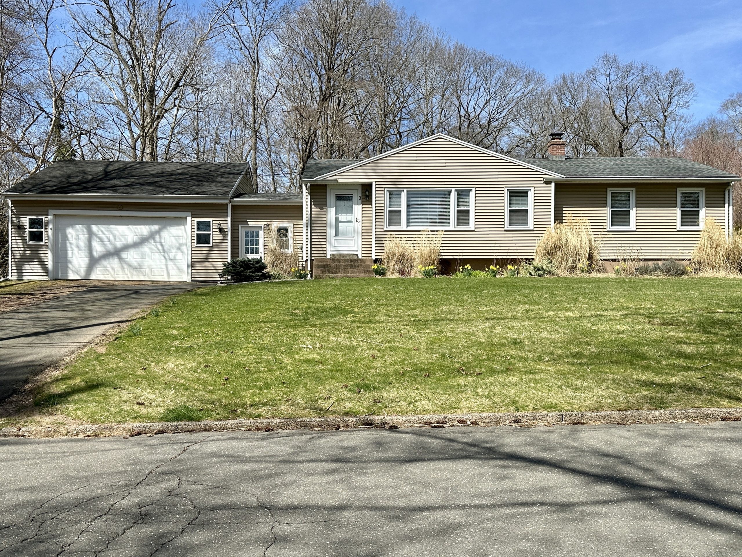 Exterior view of a beige single-story ranch home for sale in Wallingford, Connecticut, featuring an attached garage, large picture window, and a spacious green front lawn.