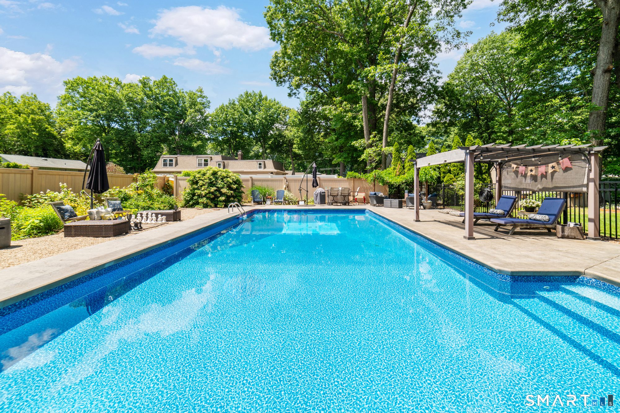Beautiful backyard oasis in Cheshire, CT, featuring a sparkling inground swimming pool with a shaded pergola and lounge area.
