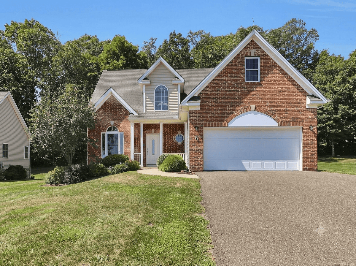 Exterior view of a single-family home with a brick facade, featuring a large arched garage door, an arched window, and a landscaped front lawn in a quiet residential setting.