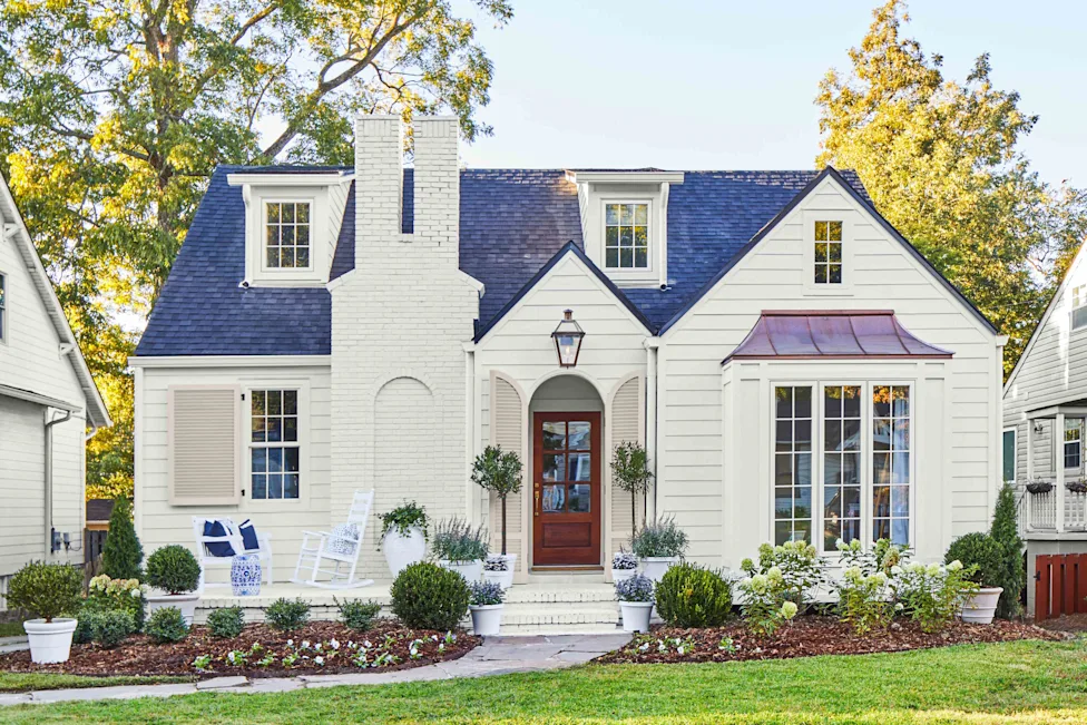A beautifully updated white cottage-style home with a dark blue roof and charming front porch, featuring manicured landscaping for curb appeal.