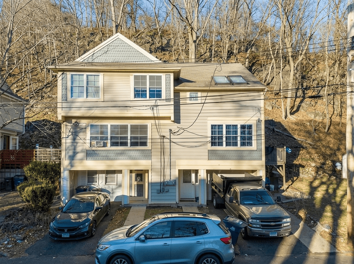 Exterior view of a family residence in New Haven, Connecticut, featuring beige siding, green shingle accents, a multi-level layout, and parking in a quiet, tree-lined setting.