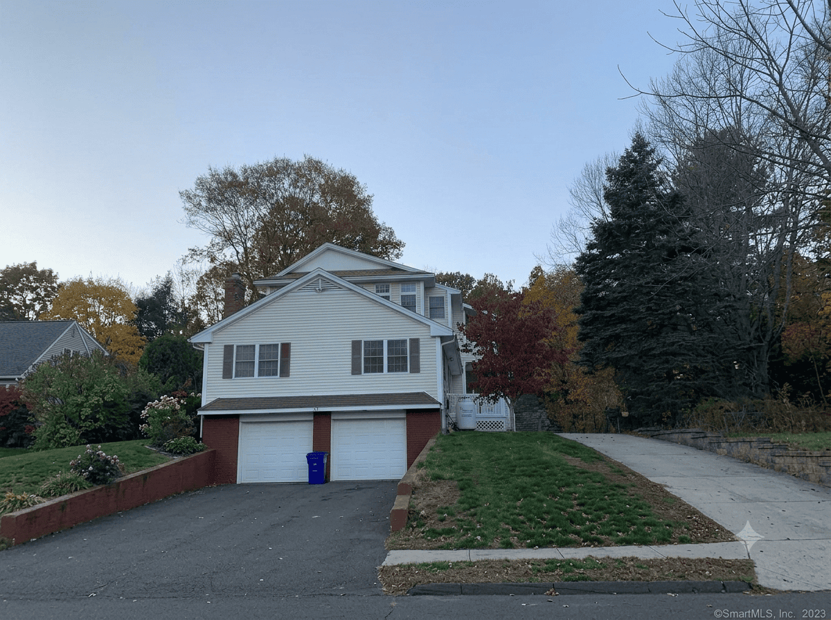 Exterior view of a multi-level home for sale featuring an attached two-car garage, concrete driveway, and established landscaping.