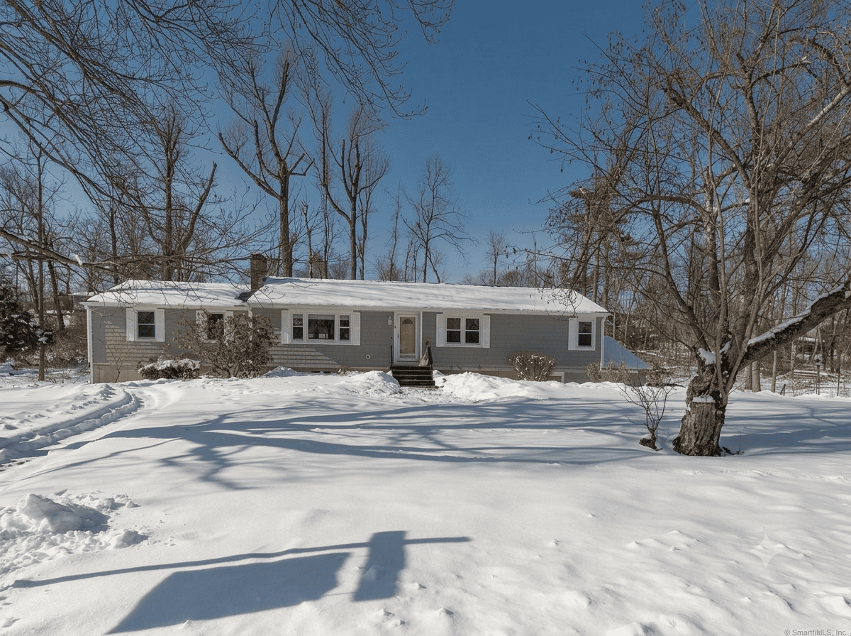 Exterior view of a winter-ready ranch-style home for sale in Hamden, CT, featuring classic grey siding, a snow-covered lawn, and a peaceful, tree-lined setting.