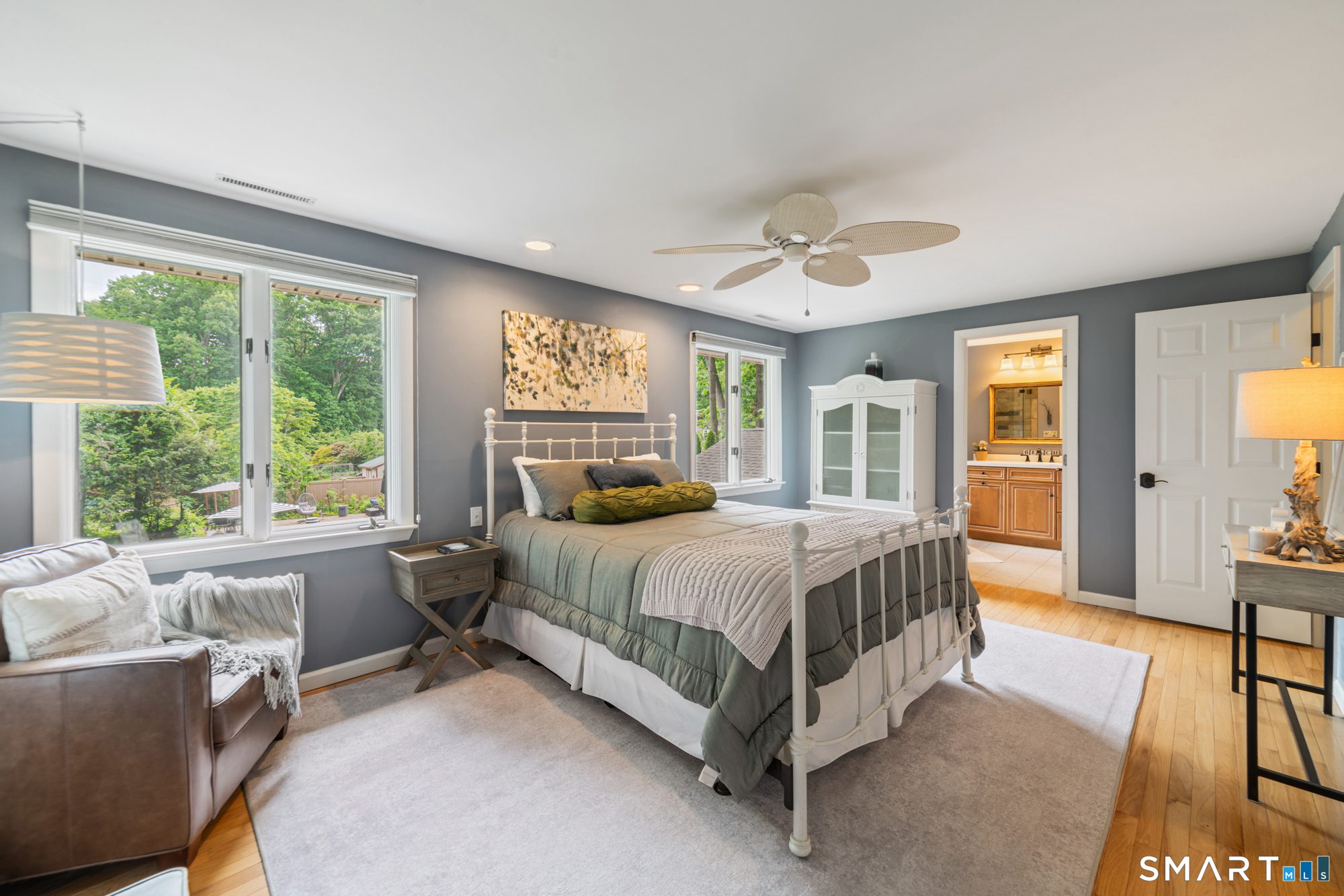 Bright and airy primary bedroom featuring a large window, white bed frame, plush gray bedding, and ensuite bathroom access.