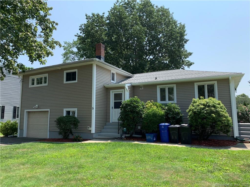 Exterior view of a beige split-level single-family home for sale, featuring an attached garage, landscaped front yard, and a classic suburban design.