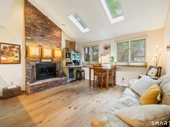Sun-filled den featuring skylights, a brick fireplace, hardwood floors, and a small dining nook.