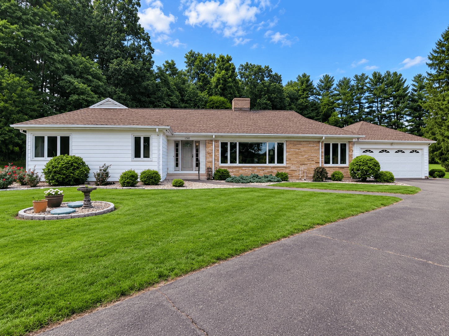 Front exterior of a well-maintained ranch-style home with an attached two-car garage, landscaped lawn, paved driveway, and mature trees.